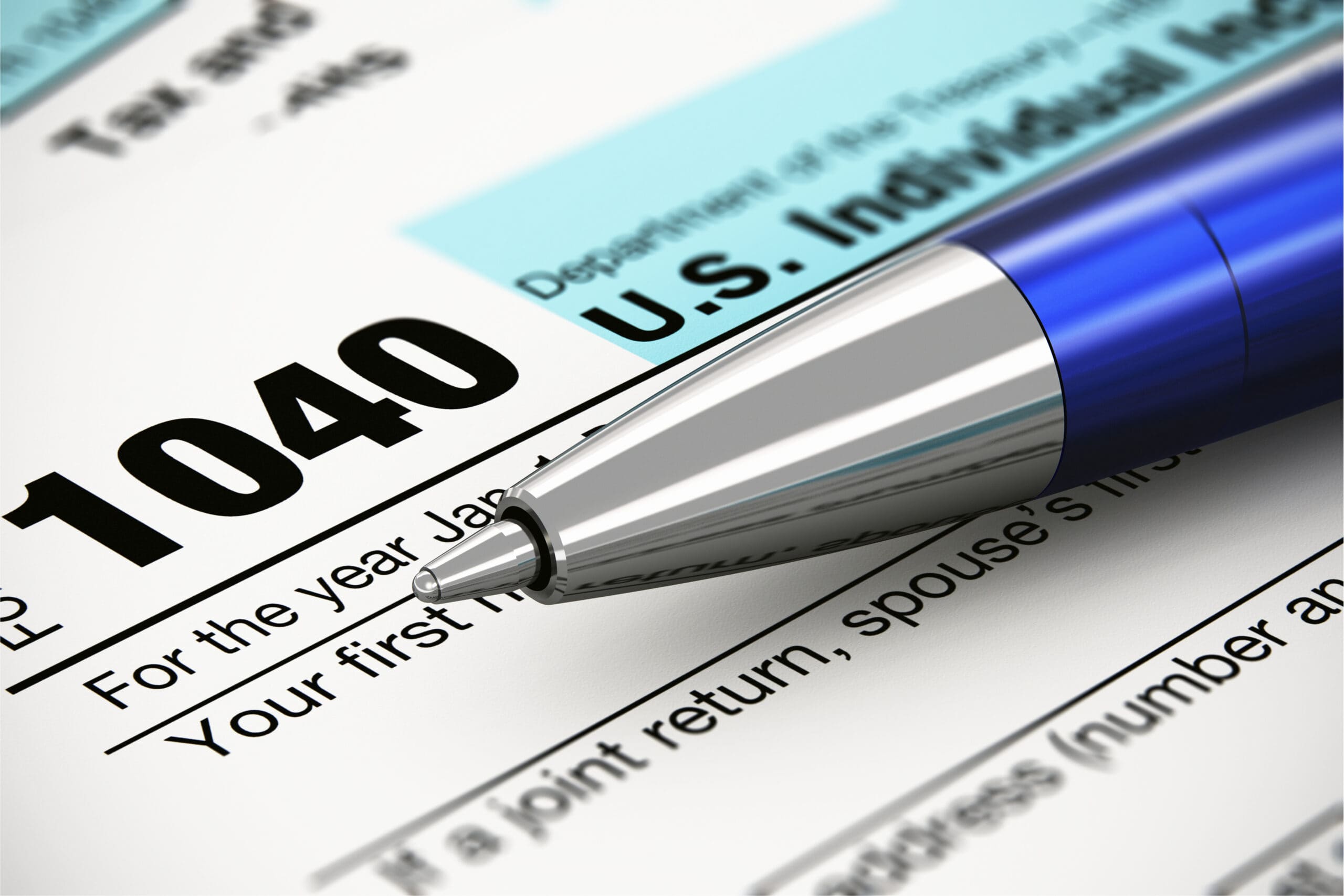 Form 1040 with a blue ballpoint pen resting on it, close-up of the pen tip and bold "1040" text on the tax paper.
